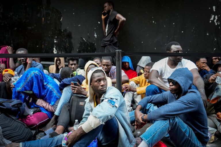 Immigrants sit in a queue outside of the Roosevelt Hotel that is being used by the city as temporary housing, July 31, 2023, in New York.