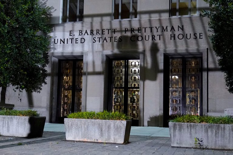 A worker carrying a metal barricade casts a shadow; barricades are installed outside the E. Barrett Prettyman U.S. Federal Courthouse, Wednesday, Aug. 2, 2023, in Washington. 
