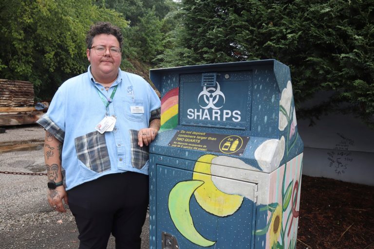 Iris Sidikman, harm reduction coordinator at the Womenâs Health Center of West Virginia, poses for a portrait beside a syringe disposal box in the clinic parking lot on Thursday, August 4, 2023, in Charleston, W.Va. 