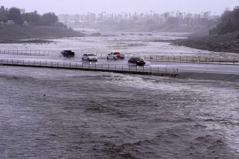 Vehicles cross over a flood control basin that has almost reached the street, Sunday, Aug. 20, 2023, in Palm Desert, Calif. Forecasters said Tropical Storm Hilary was the first tropical storm to hit Southern California in 84 years, bringing the potential for flash floods, mudslides, isolated tornadoes, high winds and power outages. 