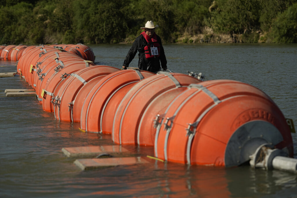 A kayaker walks past large buoys being used as a floating border barrier on the Rio Grande.
