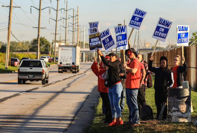 United Auto Workers, including Joseph Burch, wearing a mask, hold signs while on strike Friday, Sept. 15, 2023, at the Stellantis Toledo Assembly Complex in Toledo, Ohio.