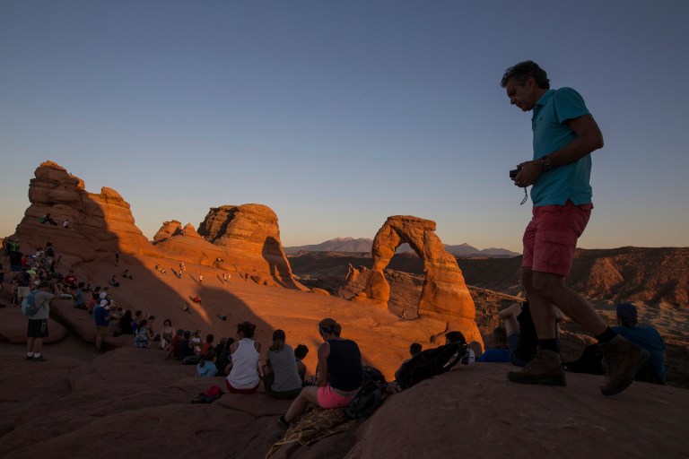 FILE - People gather to watch the sunset at Delicate Arch in Arches National Park near Moab, Utah.