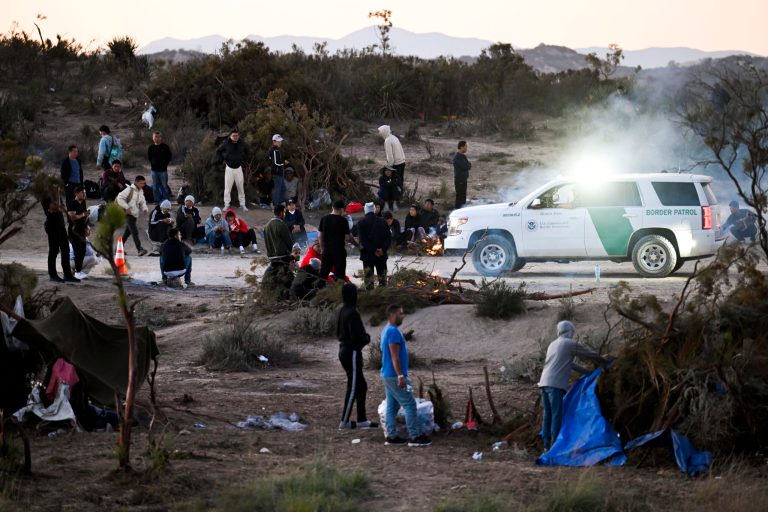 A U.S. Border Patrol agent in a vehicle watches a group of asylum-seekers at a camp after they crossed the nearby border with Mexico, Tuesday, Sept. 26, 2023, near Jacumba Hot Springs, California.