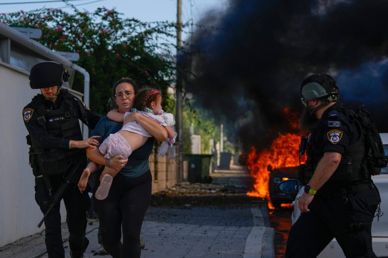 Police officers evacuate a woman and a child from a site hit by a rocket fired from the Gaza Strip, in Ashkelon, southern Israel, Saturday, Oct. 7, 2023. 