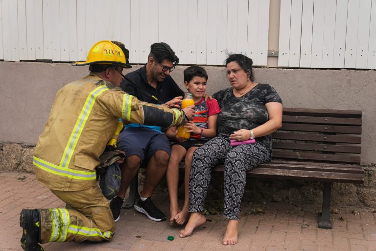 An Israeli firefighter hands a drink to a young child next to a site struck by a rocket fired from the Gaza Strip, in Ashkelon, southern Israel, Monday, Oct. 9, 2023.