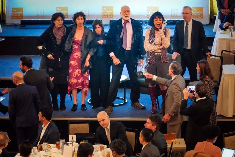 A man, third from right, throws water on climate activists protesting on a stage before Federal Reserve Chairman Jerome Powell speaks at a meeting of the Economic Club of New York on Thursday, Oct. 19, 2023, in New York. 