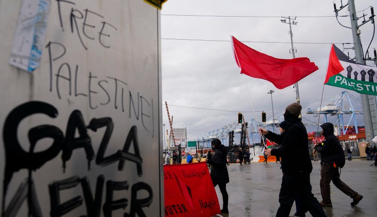 Protesters carry flags as they march past an electrical box tagged with messages like 