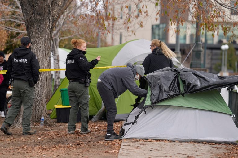 A person collects items from a tent as Denver Parks Department rangers string police tape during a city-sponsored sweep of an encampment overlooking the city skyline on Diamond Hill on Wednesday, Nov. 1, 2023, in Denver. The sweep was just one of several staged in various locations across the Mile High City.