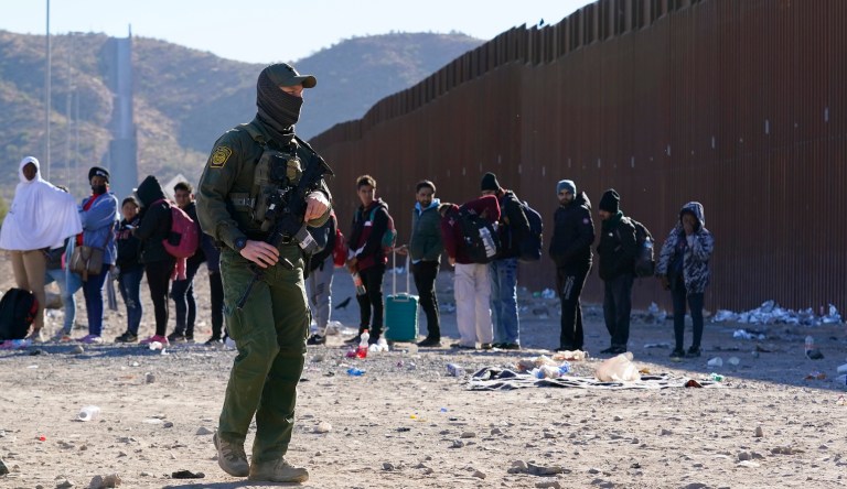 A member of U.S. Customs and Border Protection walks past a group of immigrants along the border Tuesday, Dec. 5, 2023, in Lukeville, Arizona.