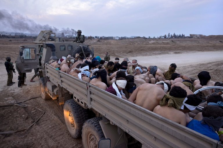 Israeli soldiers stand by a truck packed with bound and blindfolded Palestinian detainees, in Gaza, Friday, Dec. 8, 2023. Israeli forces have been rounding up Palestinians in northern Gaza for interrogation as they search for Hamas fighters.
