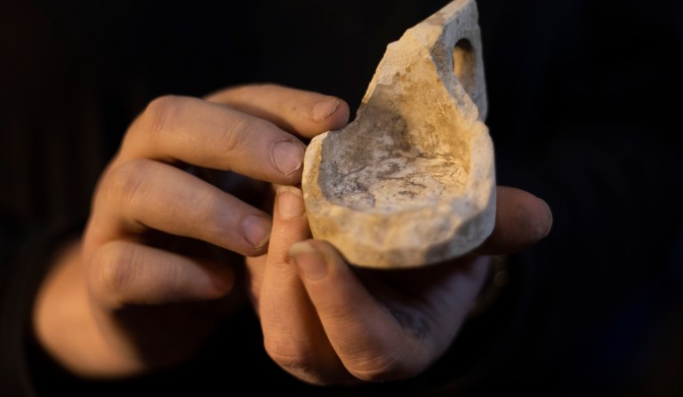 An Israel Antiquities Authority archaeologist holds a chalk measuring cup from early Roman period at an excavation site beneath the Western Wall, in Jerusalem's Old City, Tuesday, May 19, 2020. Israeli archaeologists excavating in Jerusalem exhibited a recently uncovered, unusual series of 2,000-year-old chambers carved out of the bedrock beneath the Western Wall plaza on Tuesday. The excavations are uncovering new sections of a sprawling network of ancient subterranean passageways running alongside a contested Jerusalem holy site known to Jews as the Temple Mount and to Muslims as the Noble Sanctuary.
