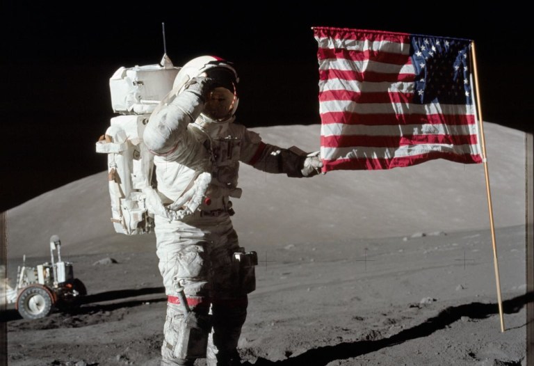 Astronaut Eugene A. Cernan, Apollo 17 commander, is photographed next to the deployed United States flag during lunar surface extravehicular activity (EVA) at the Taurus-Littrow landing site. The highest part of the flag appears to point toward our planet Earth in the distant background. This picture was taken by scientist-astronaut Harrison H. Schmitt, lunar module pilot. While astronauts Cernan and Schmitt descended in the Lunar Module (LM) to explore the moon, astronaut Ronald E. Evans, command module pilot, remained with the Command and Service Modules (CSM) in lunar orbit.