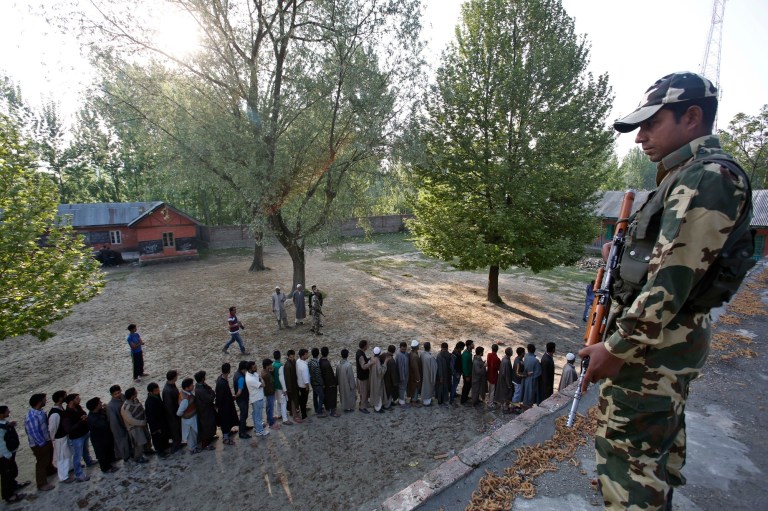 An Indian paramilitary soldier guards as Kashmiri villagers line-up to cast their votes during the eighth phase of voting of the Indian parliamentary elections at Panzinar, 28 kilometers (17.5 miles) north of Srinagar, India, Wednesday, May 7, 2014. The multiphase voting across the country runs until May 12, with results for the 543-seat lower house of parliament expected on May 16. (AP Photo/Mukhtar Khan)