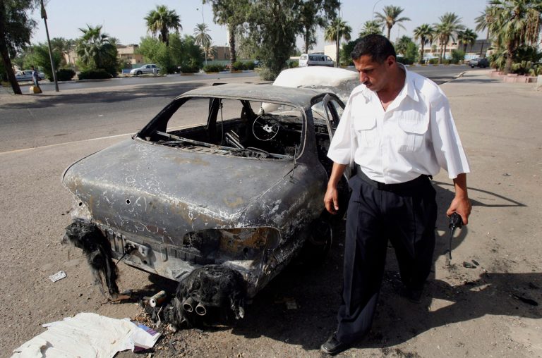FILE - This Sept. 25, 2007 file photo shows an Iraqi traffic policeman inspecting a car destroyed by a Blackwater security detail in al-Nisoor Square in Baghdad, Iraq.  In a tale of death and destruction, a federal prosecutor has chronicled for a jury the alleged conduct of four Blackwater security guards accused of killing 14 Iraqis and wounding 18 others in downtown Baghdad nearly seven years ago. In opening statements Tuesday at the trial of the four guards, Assistant U.S. Attorney T. Patrick Martin said the victims were simply trying to get out of the way of gunfire from the Blackwater guards. (AP Photo/Khalid Mohammed, File)