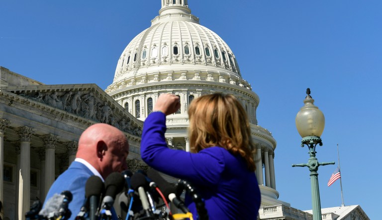 With the flag flying at half-staff for the victims of the Las Vegas shootings, former Rep. Gabrielle Giffords, D-Ariz., shakes her fist at the United States Capitol as she and her husband Mark Kelly speak about the mass shooting in Las Vegas. (AP Photo/Susan Walsh)