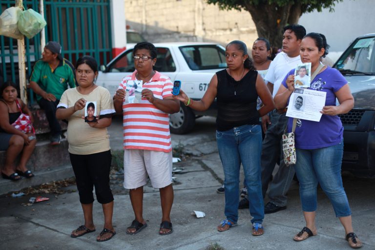People hold portraits of their missing loved ones in front of the morgue of Cosamaloapan, with the hope of finding and identifying the bodies of their missing, from a mass grave which has been recently discovered, in Veracruz , Mexico, Wednesday, June 18, 2014. At least 28 bodies have been recovered from the mass grave in Veracruz, an eastern Mexican state plagued by attacks on migrants and drug cartel violence, officials said Wednesday. (AP Photo/Felix Marquez)
