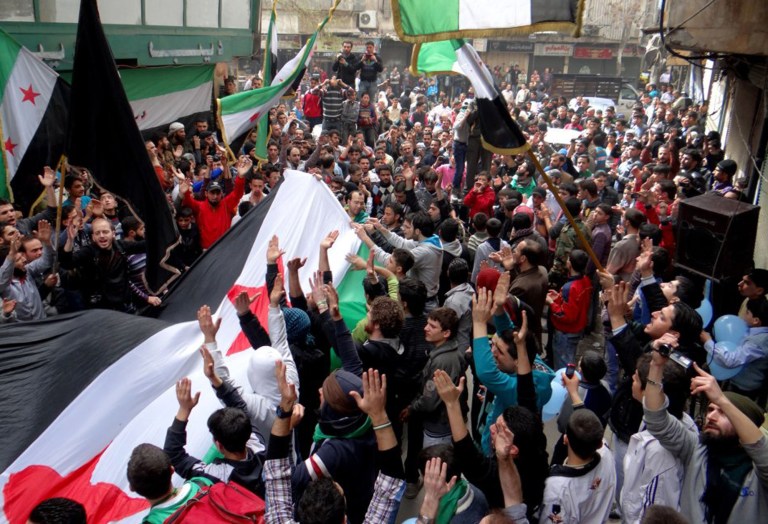 In this citizen journalism image provided by Aleppo Media Center AMC which has been authenticated based on its contents and other AP reporting, anti-Syrian regime protesters raise up their hands as they wave Syrian revolutionary flags during a protest to mark the second anniversary of the their uprising, in Aleppo, Syria, Friday March 15, 2013. The chief of Syria's main, western-backed rebel group marked the second anniversary of the start of the uprising against President Bashar Assad on Friday by pledging to fight until the 