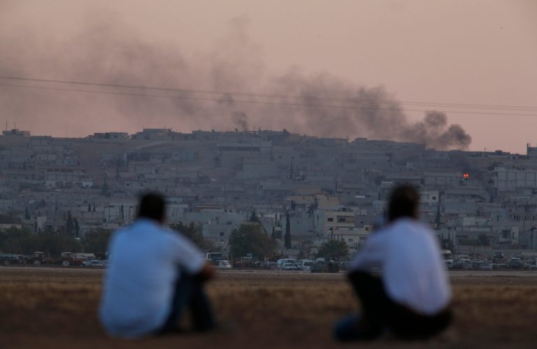 Turkish Kurds sit on the outskirts of Suruc, on the Turkey-Syria border, and watch smoke rise following an airstrike in Kobani, Syria, on Tuesday. (AP/Lefteris Pitarakis)