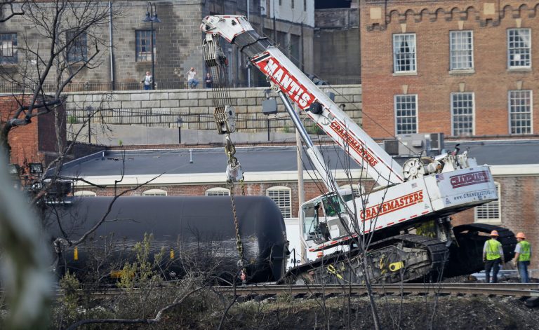 Workers remove damaged tanker cars along the tracks where several CSX tanker cars carrying crude oil derailed and caught fire along the James River near downtown Lynchburg, Va., Thursday, May 1, 2014.  Virginia state officials were still trying Thursday to determine the environmental impact of the train derailment.  (AP Photo/Steve Helber)