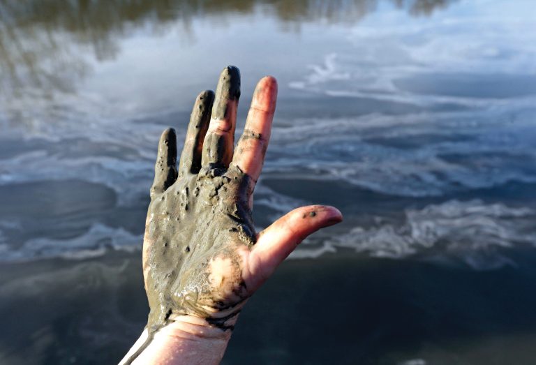 Amy Adams, North Carolina campaign coordinator with Appalachian Voices, shows her hand covered with wet coal ash from the Dan River swirling in the background as state and federal environmental officials continued their investigations of a spill of coal ash into the river in Danville, Va., on Feb. 5. (AP Photo/Gerry Broome)