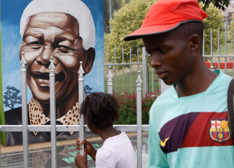 A child looks through a fence at a portrait of former president Nelson Mandela in a Park in Soweto, South Africa, Thursday, March, 28, 2013. 94-year-old Mandela, the anti-apartheid leader who became South Africa's first black president, has been hit by a lung infection again and is in a hospital, the presidency said. Mandela, has become increasingly frail in recent years and has been hospitalized several times in recent months, including earlier this month when he underwent what authorities said was a scheduled medical test. The Nobel laureate is a revered figure in South Africa, which has honored his legacy of reconciliation by naming buildings and other places after him and printing his image on national banknotes. (AP Photo/Denis Farrell)
