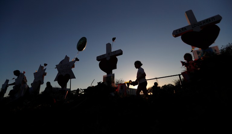 People walk among a makeshift memorial outside the Marjory Stoneman Douglas High School, where 17 students and faculty were killed in a mass shooting in Parkland, Fla., Sunday, Feb. 18, 2018. (AP Photo/Gerald Herbert)