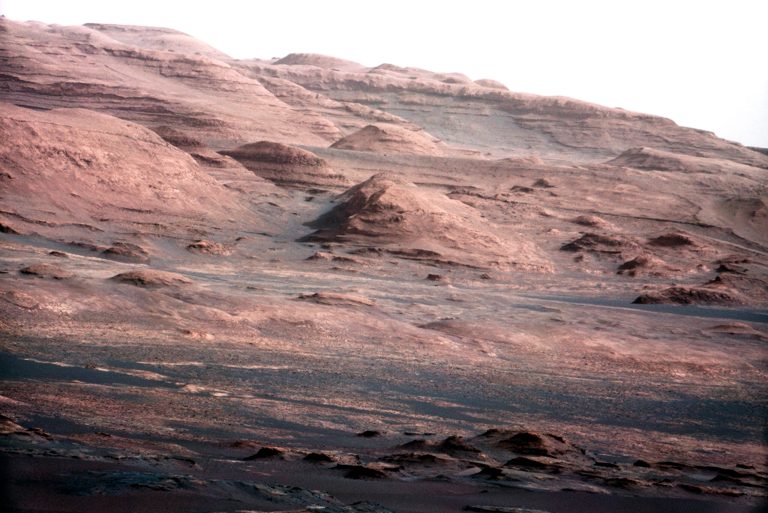 In this image released by NASA on Monday, Aug. 27, 2012, a chapter of the layered geological history of Mars is laid bare in this color image from NASA's Curiosity rover showing the base of Mount Sharp, the rover's eventual science destination. The image is a portion of a larger image taken by Curiosity's 100-millimeter Mast Camera on Aug. 23, 2012. Scientists enhanced the color in one version to show the Martian scene under the lighting conditions we have on Earth, which helps in analyzing the terrain. The pointy mound in the center of the image, looming above the rover-sized rock, is about 1,000 feet (300 meters) across and 300 feet (100 meters) high.