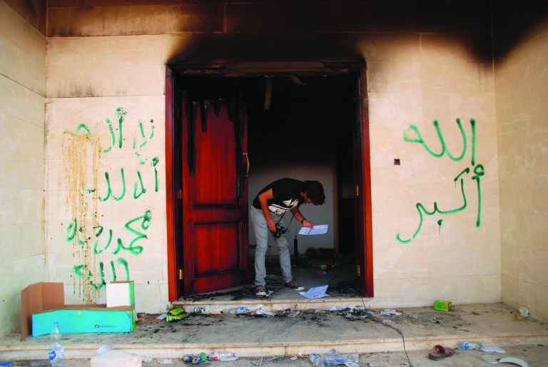 FILE - On this Wednesday, Sept. 12, 2012 file photo, a man looks at documents at the U.S. consulate in Benghazi, Libya, after an attack that killed four Americans, including Ambassador Chris Stevens. The graffiti reads, 