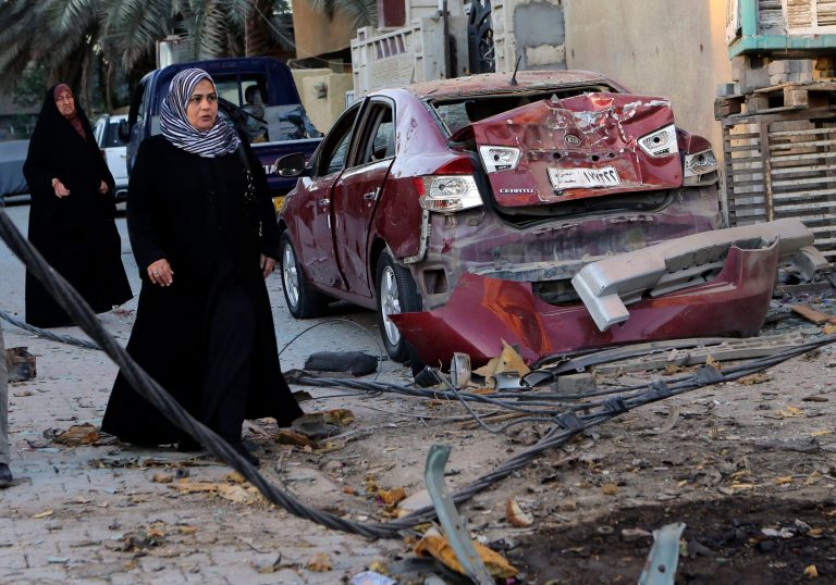 Women walk past the aftermath of a car bomb attack in the mainly Shiite neighborhood of Zafaraniyah in southeastern Baghdad, Iraq, on Oct. 8. (AP/Hadi Mizban)