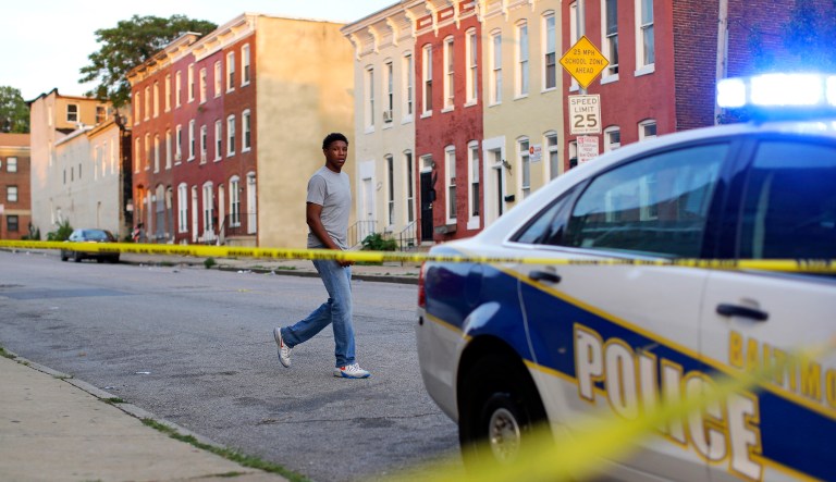 In this July 30, 2015 picture, a man walks past a corner where a victim of a shooting was discovered in Baltimore.
