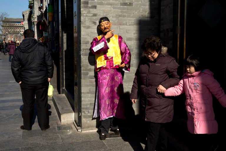 A woman drags her granddaughter away from a shop near an advertising mascot while a man, left, waits for customers at the entrance of a restaurant on a shopping street in Beijing, China, Thursday, Jan. 30, 2014. The reluctance of customers to open their wallets wider is one of a thicket of obstacles facing communist leaders as they try to rebalance Chinaâs economy away from reliance on investment that is losing its ability to boost growth. (AP Photo/Alexander F. Yuan)