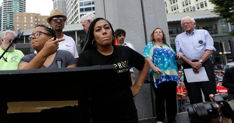 Marissa Johnson, left, and Mara Jacqueline Willaford refuse to stand down after taking over the podium from Democratic presidential candidate Sen. Bernie Sanders. (AP Photo/Elaine Thompson)
