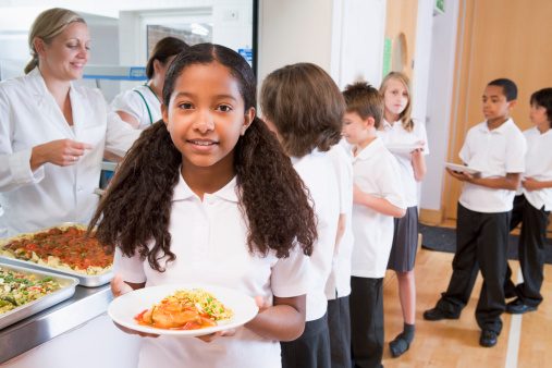 Schoolgirl holding plate of lunch in school cafeteria