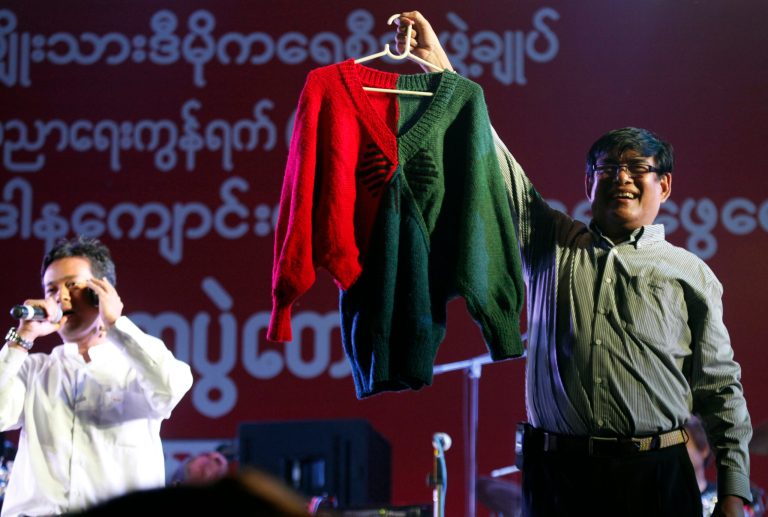   In this Thursday, Dec. 27, 2012 photo, presenters show a hand-knit woolen sweater, made by Myanmar opposition leader Aung San Suu kyi, during an auction at a fundraising concert to mark the 2nd anniversary of her National League for Democracy Party's education network, at Peoples Square in Yangon, Myanmar. The sweater was sold at an auction in Myanmar for almost $50,000. (AP Photo/Khin Maung Win)  