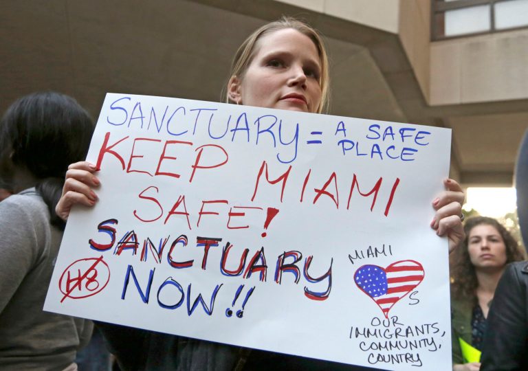 Protester Jennifer Smith-Camejo holds a sign during an anti-Trump and anti-Gimenez rally in downtown Miami. Tuesday, Jan. 31, 2017. Miami-Dade County Mayor Carlos Gimenez issued a controversial order last week assuring the Trump administration that Miami-Dade is not functioning as a sanctuary city for illegal immigrants. (AP Photo/Alan Diaz)
