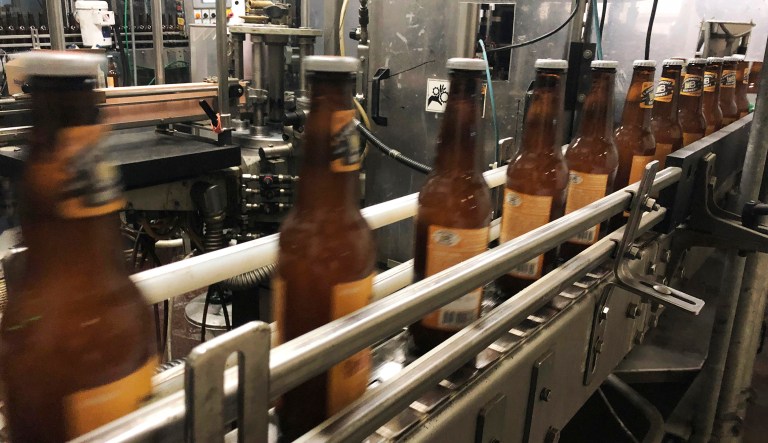 In this Jan. 14, 2019, photo, bottles, freshly filled with beer, move on a belt at Lakefront Brewery in Milwaukee. The federal shutdown is impacting the federal agency Alcohol and Tobacco Tax and Trade Bureau, which approves licenses for new breweries, some ingredients and labels for beers sent out of state. The brewery is now waiting for the federal agency to approve the "My Turn: Chuck" beer label, so they can sell it out of state.