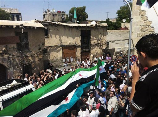 This citizen journalism image provided by Shaam News Network SNN purports to show Syrians holding a large Syrian revolutionary flag during a funeral procession in Damascus. (AP Photo)
