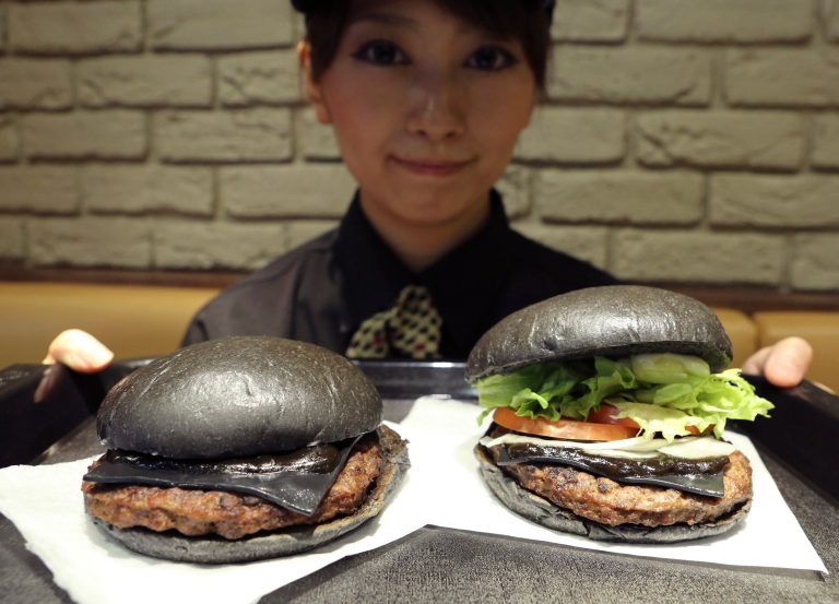 FILE - In this Sept. 16, 2014 file photo, Burger King employee Rumi Sekine shows the Kuro Diamond burger, right, and the Kuro Pearl burger at its Shibuya restaurant in Tokyo. The fast-food chain is offering customers an initially unappetizing experience as it launched two limited edition 