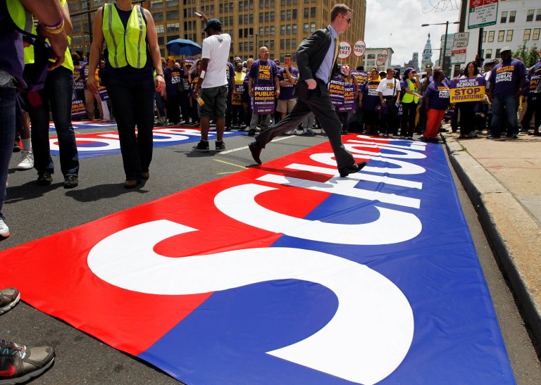   FILE-In this file photo from May 23, 2012, a man runs across a sign in the street in front of the Philadelphia School District during a protest of Pennsylvania Gov. Tom Corbett's proposed cuts to the education budget in Philadelphia. Like many other cash-strapped urban districts, Philadelphia is trying desperately to emerge from a quagmire of red ink and underachievement. A state takeover in 2002 did little to eradicate the financial, academic and violence problems that have plagued the schools for years. (AP Photo/Alex Brandon, FILE)  