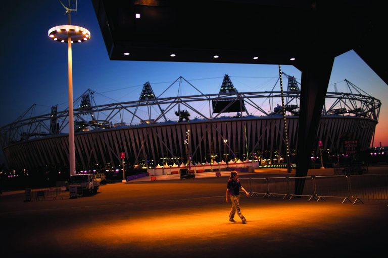 A volunteer walks past the Olympic Stadium at the 2012 Summer Olympics, Sunday, July 22, 2012, in London. The opening ceremonies of the Olympic Games are scheduled for Friday, July 27. (AP Photo/Emilio Morenatti)