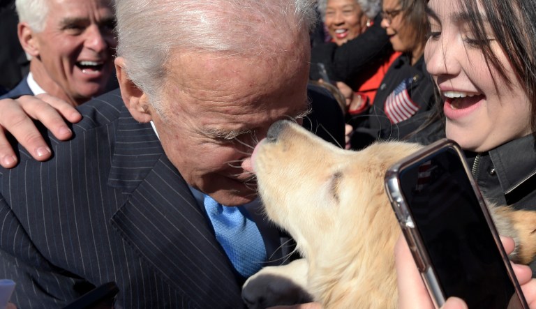 Former Vice President Joe Biden gets a kiss from a dog as he greets the crowd on Capitol Hill in Washington, Wednesday, March 22, 2017, following an event marking seven years since former President Barack Obama signed the Affordable Care Act into law.