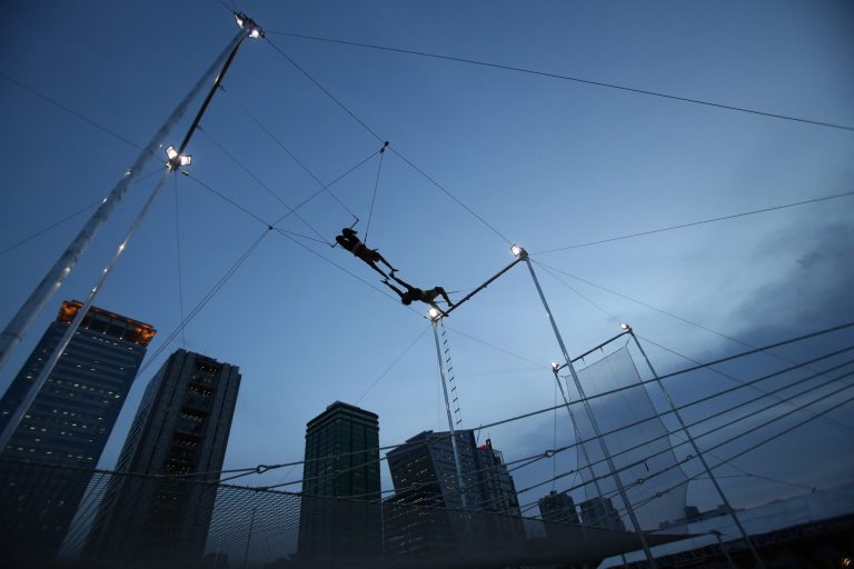 In this photo taken Tuesday, Aug. 12, 2014, flying trapeze instructor and school owner William Hsu, right, catches one of his students during their first day of practice at the Flying Trapeze Philippines School in suburban Makati, south of Manila, Philippines. The new facility teaches students basic techniques from taking off a platform as high as a three-story building, hanging on to the swinging trapeze bar with your hands or back of knees and landing on the safety net below said Hsu. He added that the thrilling activity has gained adherents, with about 150 to 200 such flying trapeze training facilities now in existence worldwide. (AP Photo/Aaron Favila)
