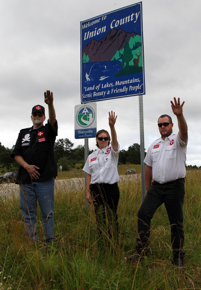   From left, Knighthawk, April Hanson and her husband Harley Hanson, members of the International Keystone Knights Realm of Georgia, perform a traditional Klan salute along the portion of highway they want to adopt allowing them to put up a sign and do litter removal near Blairsville, Ga., Sunday, June 10, 2012. The Ku Klux Klan group wants to join Georgia's 