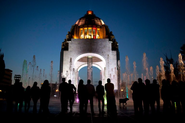   Pedestrians stand in front of the Arch of the Revolution monument in Mexico City, Wednesday, Dec. 26, 2012. The once-neglected plaza with an Arc de Triumph-style monument to Mexico's 1910 revolution has been remade from a homeless encampment to a place where families visit and children run through spurts of water gushing out of the pavement. The copper dome of what started out as the congressional rotunda is newly polished and gleaming. Mexico City's government is trying to transform one of the world's largest cities by beautifying public spaces, parks and monuments. (AP Photo/Alexandre Meneghini)  