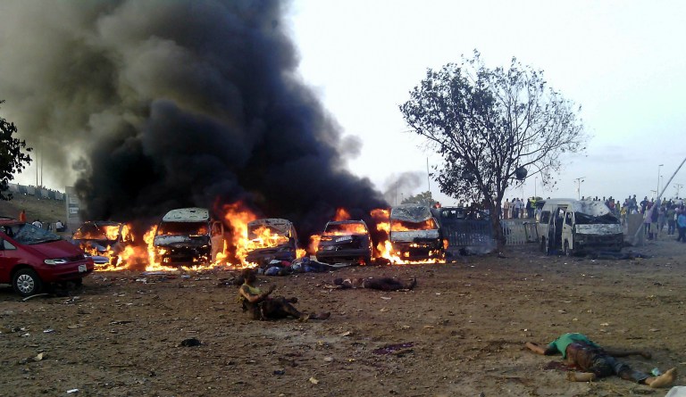 Victims of a blast lie on the ground as fire and smoke rise at a bus park in Abuja, Nigeria, Monday, April 14, 2014. A massive explosion ripped through a bus station during the morning rush hour in Nigeria's capital, killing and wounding scores of people in a bombing that marked the bloodiest terrorist attack ever in Abuja. (AP Photo/Kayode Olamikan)