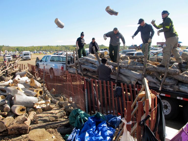 In this Wednesday, Sept. 14, 2016, photo, volunteers toss logs at an oil pipeline protest encampment near the Standing Rock Sioux Reservation in southern North Dakota. The logs will be used to cook meals for the thousands of people who have come to the area to fight the $3.8 billion Dakota Access pipeline. (AP Photo/James MacPherson).