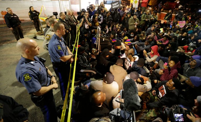 Protesters sit silent for over four minutes at the Ferguson Police Department Saturday, Oct. 11, 2014, during a rally in remembrance of Michael Brown in Ferguson, Mo. (AP Photo/Charles Rex Arbogast)