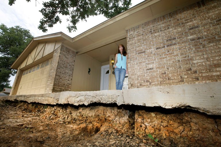 Barbara Brown poses for a photo on the front step of her home that now sits about one foot off the surface of her lawn, Saturday, June 21, 2014, in Reno, Texas. Brown said that the top of the step once sat about four inches off the surface of her lawn. Brown said she believes the sinkholes on her property and the drop of her lawn have to do with natural gas drilling. (AP Photo/Tony Gutierrez)