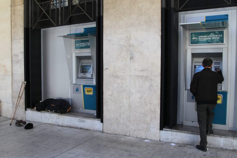 A person with disabilities sleeps next to ATM of National bank branch as a customer transacts in the northern Greek port of Thessaloniki, Wednesday, Jan. 29, 2014. (AP Photo/Nikolas Giakoumidis)